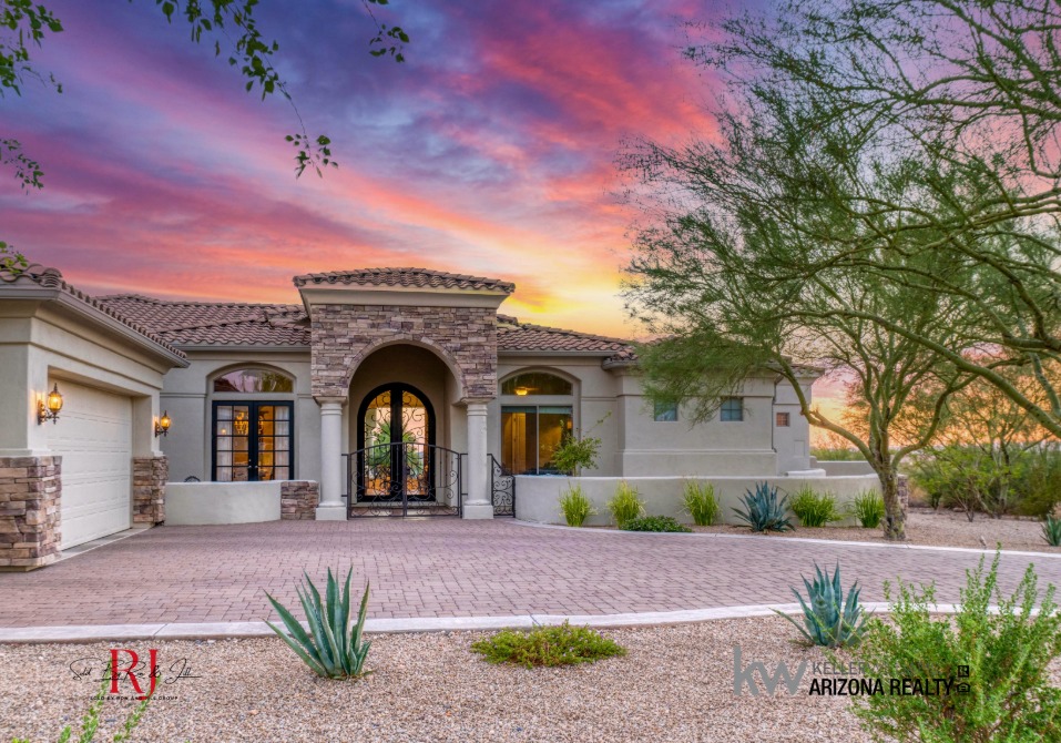 Arch 002 - Sold By Ron And Jill Group - Sold By Ron And Jill Group Elegant desert-style home with a stone archway entry and brick driveway at sunset.