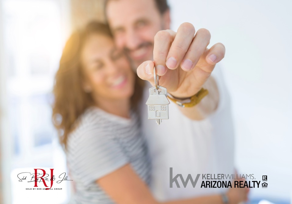 Happy Couple 002 - Sold By Ron And Jill Group - Sold By Ron And Jill Group Smiling couple holding up a silver house key toward the camera, symbolizing a new home purchase (real estate ad).