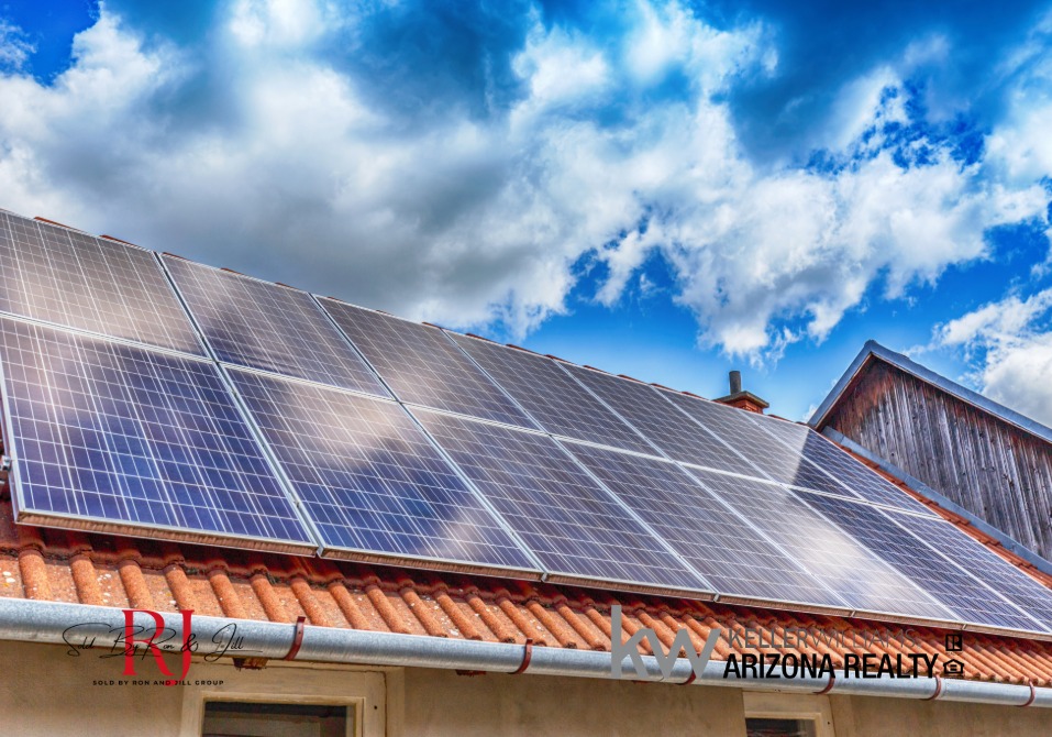 Solar panels on a red-tiled roof under a blue, cloudy sky; real estate signage visible in the bottom-right corner.